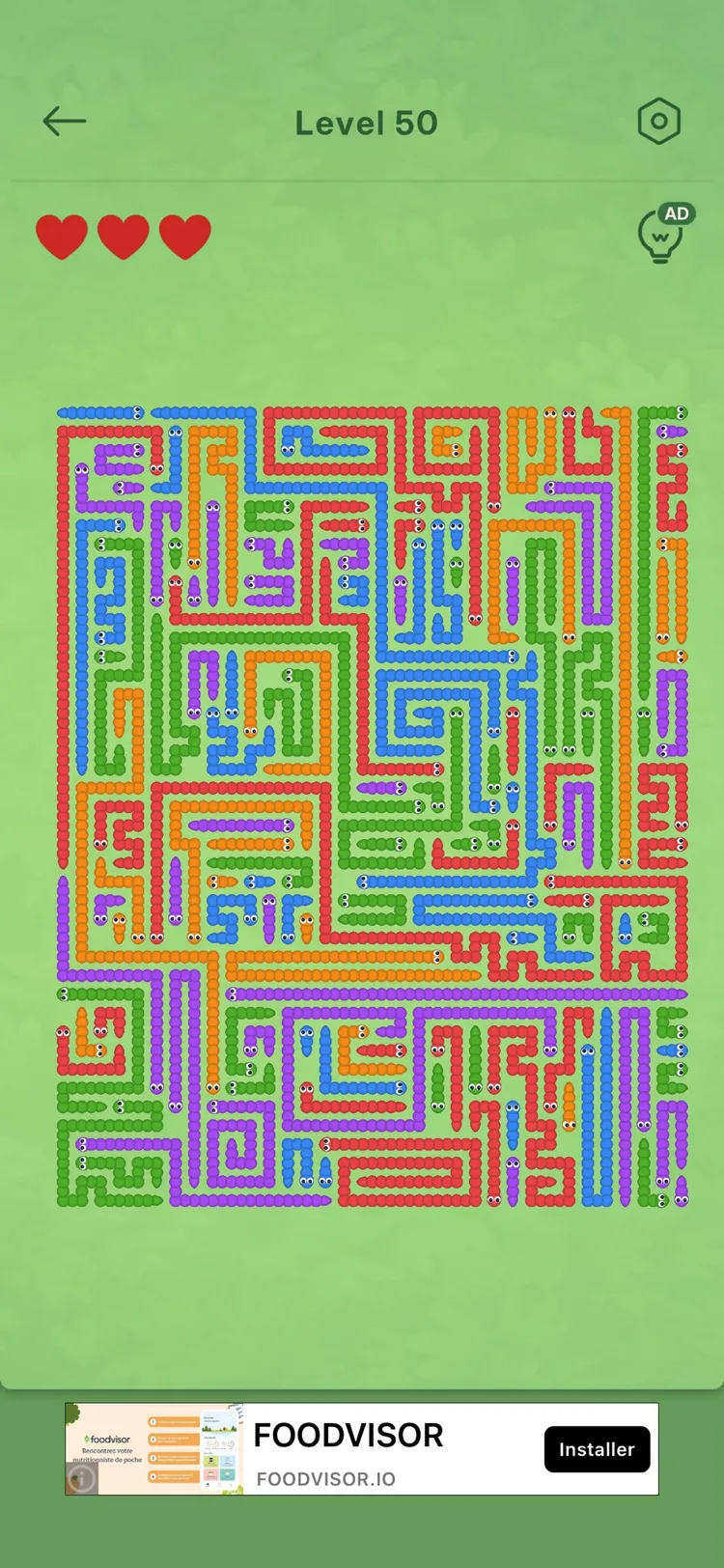 A crowded caterpillar level in Amaze Go: a green board packed edge to edge with red, orange, blue, green and purple caterpillars, each with a little face